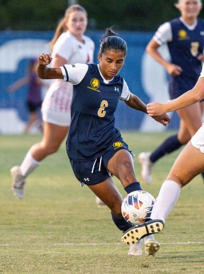 Soccer player kicks the ball as opponent tries to block.